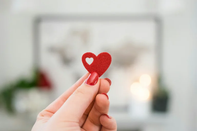 Nell'immagine una mano di donna con delle unghie rosse regge un cuoricino di feltro anch'esso rosso.