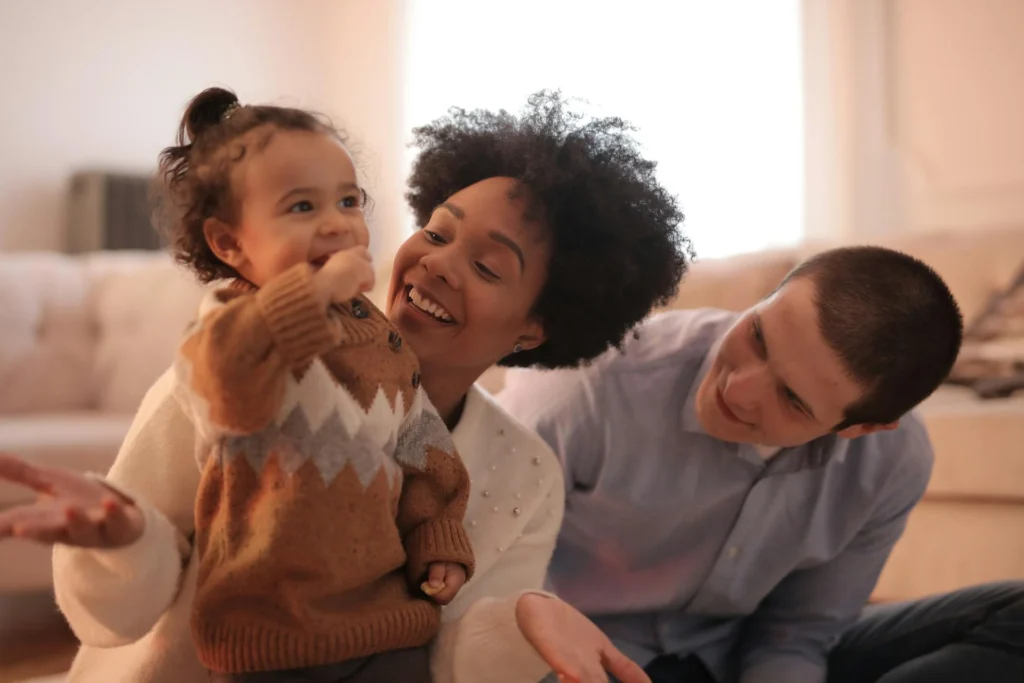 Nell'immagine si vede una famiglia composta da mamma, papà e figlia. I genitori sorridenti guardano la bambina che sgranocchia un pezzetto di biscotto.