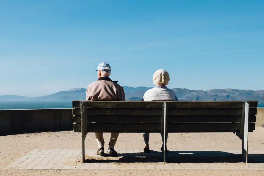 Nell'immagine, si vede una coppia di persone anziane di spalle, sedute su una panchina a guardare il panorama.