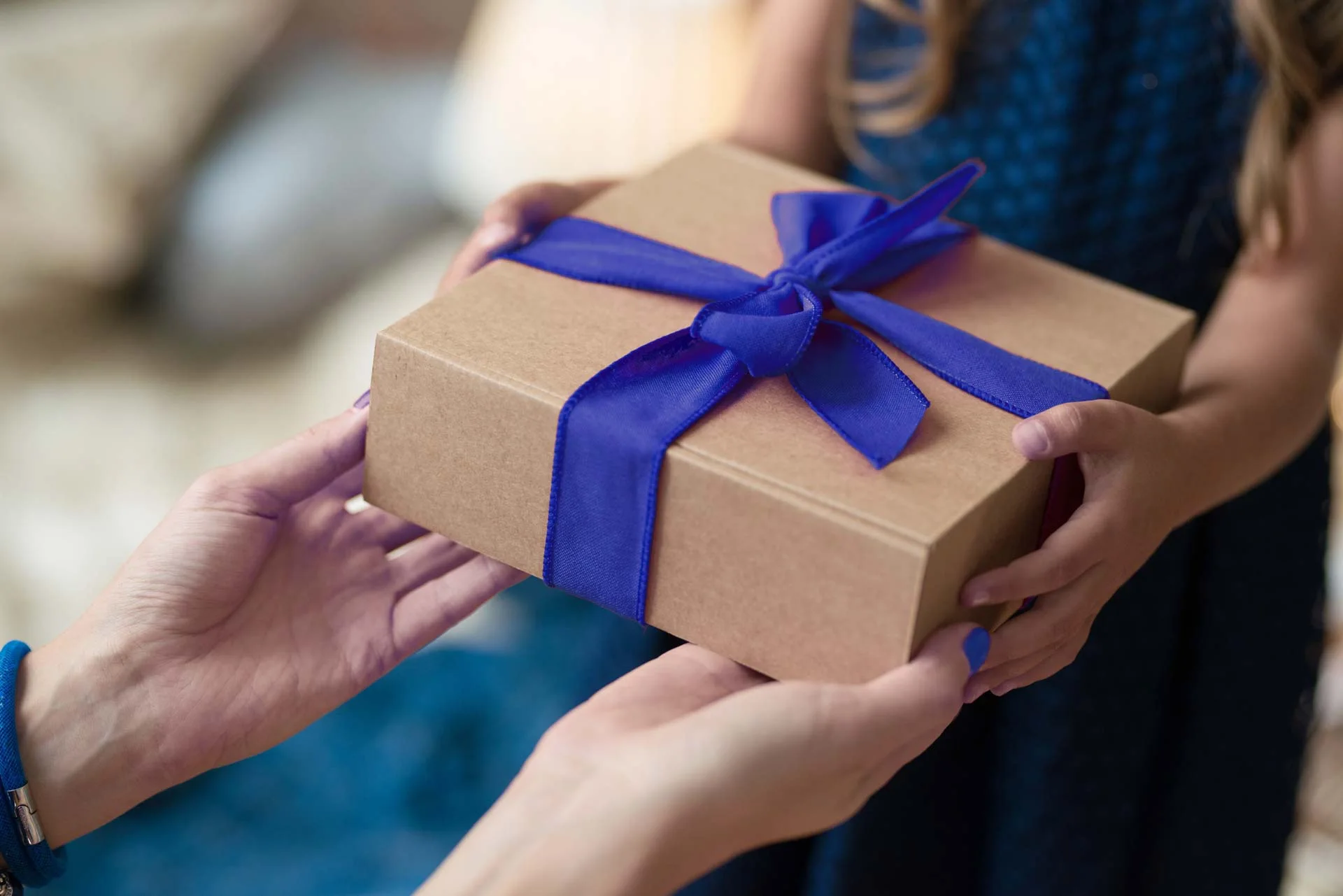 In the image two people are exchanging a gift package. The package is brown with a large blue bow.