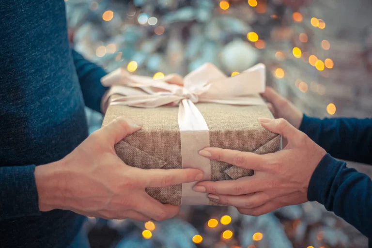 Nell'immagine, il primo piano delle mani di due persone che si scambiano un pacco regalo.