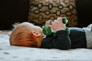 In the picture, the close-up of a baby on a bed holding a plush in his hands.